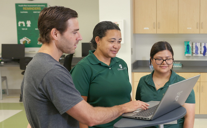 Photo of three staff members looking at a laptop computer.